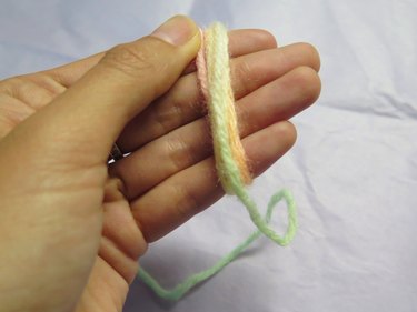 Wrapping a string of yarn around fingers for a DIY pompom bookmark