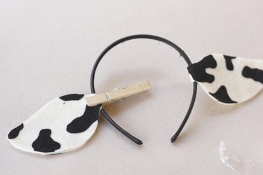 ...Two fabric cow ears are attached to a black headband; one is held with a clothespin