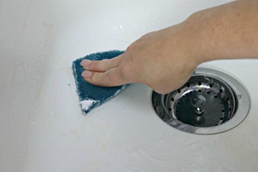 Scrubbing white kitchen sink with cleaner
