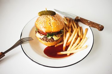 Beef hamburger a brioche bun on a plate with French fries and ketchup.