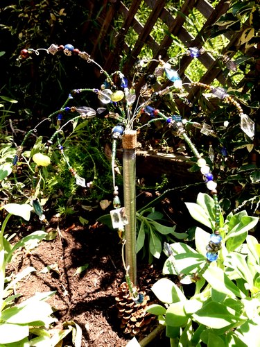 DIY glass beaded garden sparkler in soil among plants.