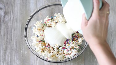 pouring melted white chocolate over popcorn and sprinkles