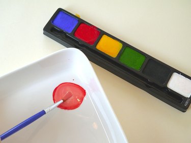 A face paint palette and a brush mixing peach.