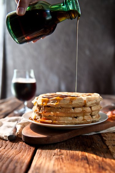 Maple syrup being poured over a stack of waffles.