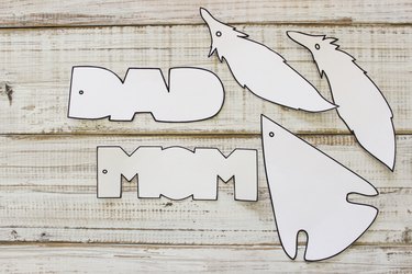 Printed and cut out air freshener designs: capital, block letters spelling "DAD" and "MOM", an arrowhead, and 2 feathers.