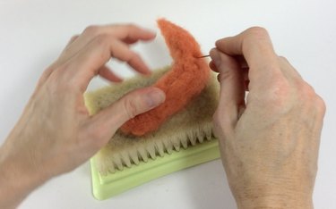 Female hands needle felting orange roving on a felting pad