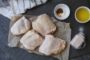 chicken thighs, salt, oil, and seasoning on a cutting board
