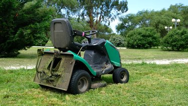Green grass trimming with lawn mower. Tractor mowing grass in a public park. A dirty lawn tractor after mowing the lawn stands on the meadow. Professional lawn mower cuts the grass.