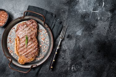 Barbecue Grilled striploin or New York beef meat steak with pink salt and herbs. Black background. Top view. Copy space