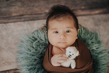 Little baby boy with knitted hat in a basket, happily smiling and looking at camera, isolated studio shot