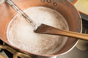 boiling syrup of sugar in copper pan with thermometer and big spoon
