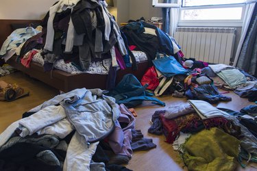 Clothes and other objects scattered on floor and bed