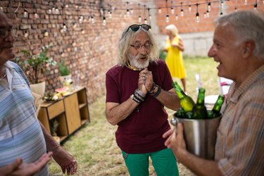 Senior man is happy to see his friend bringing beer on party at backyard