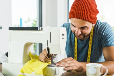 Young man at home using sewing machine