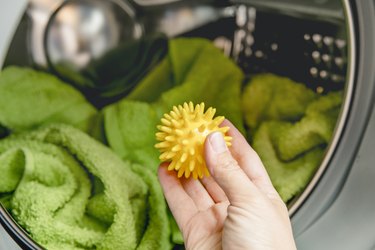 Using pvc dryer balls is natural alternative to both dryer sheets and liquid fabric softener, balls help prevent laundry from clumping in the dryer. Woman hand put in a yellow spiky dryer ball.
