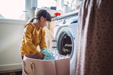Lovely little girl unloading the washing machine while helping her mom with laundry at home