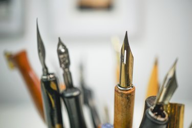 Group of wooden penholders with calligraphy nibs on a colourful mug on a table with nice background