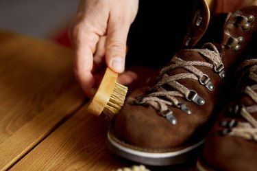 Man's hand clean suede shoes, boots with a brush on wooden background.