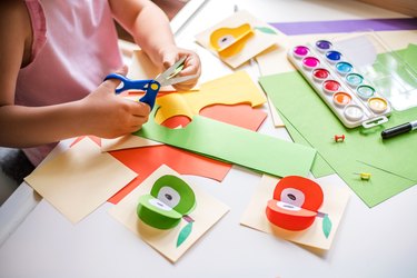 Little girl cutting colorful paper at the table.