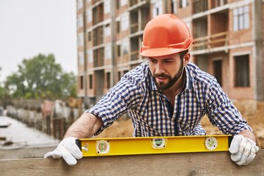 Accuracy and quality. Construction worker in protective yellow helmet checking the level of a plank of wood. Measurement concept