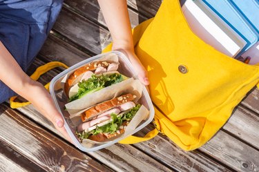 Lunch box in the hands of a child. Sandwiches in a plastic container. Snack, school breakfast. Back to school. Lunch break.Yellow backpack with books