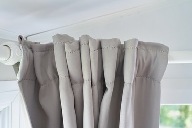 thick gray curtain hanging over white drapery inside a room on sunny day.