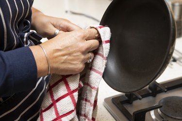 Mature female hand wiping a frying pan with a tea towel in a domestic kitchen