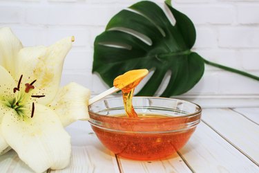 Sugar paste for hair removal in a bowl with lily flower and dracaena leaf in glass vase on white background, body care