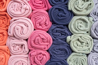 A stacked pile of rolled-up warm fleece blankets. Rolls of various color blankets lie on a shelf,  fabric on a shelf in a store.
