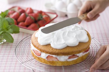 Human Hand Spreading Cream on Top of Sponge Cake