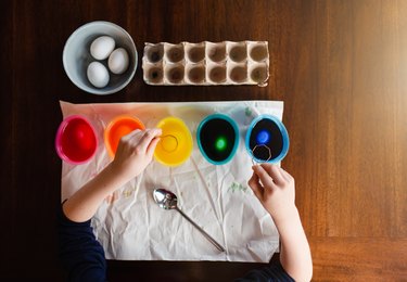 Overhead view of child's hands dying Easter eggs on wooden table.
