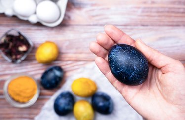 Woman's hand hold blue Easter egg. Coloring eggs for Easter with natural food coloring turmeric and hibiscus tea at home. Close-up. Top view.