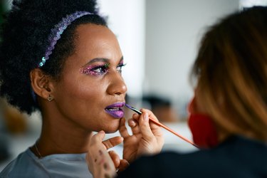 Mid adult black woman woman putting on make-up for Mardi Gras festival celebration.