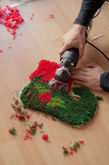Christmas elf boot decoration on pine wood parquet. Handmade rug, still unfinished. Textile craft work with natural fibers. White man's hands, Shearing, cutting off the leftover strands.