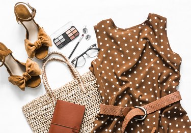 Polka dot summer brown dress, suede wedge sandals, eco straw tote bag, cosmetics on a light background, top view. Women's clothing set