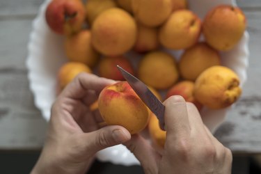 Female hands cutting fresh sweet peaches to make peach jam.