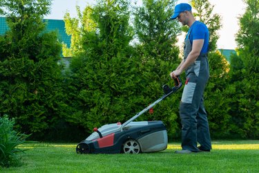 Young gardener in overalls uses a lawn mower on the plot