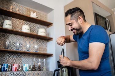 Mid adult men man opening a wine bottle in the kitchen