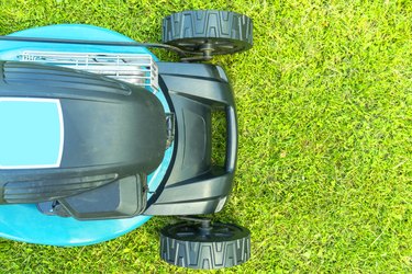 Mowing lawns. Lawn mower on green grass. Mower grass equipment. Mowing gardener care work tool close up view. Sunny day.