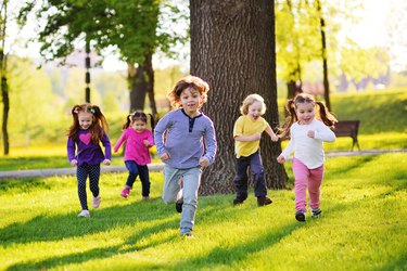 many young children smiling running along the grass in the park