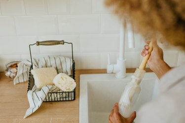 Young woman washing reusable glass bottle with natural brush