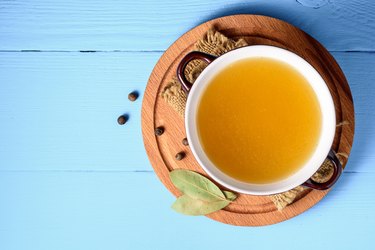Chicken broth in ceramic bowl on blue wood background