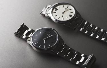 Two metallic wristwatches on gray background. Horizontal studio shot.