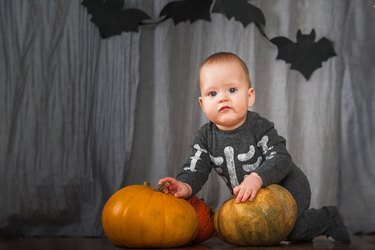 Baby 8 months with pumpkins for Halloween. Infant at home with pumpkin harvest and wearing skeleton costume...
