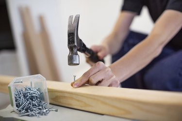Midsection of female carpenter hammering nail into wooden plank