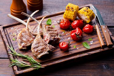 Lamb ribs grilled on cutting board with roasted vegetables.