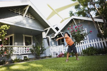 Boy flying toy airplane in front yard of house