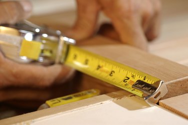 Close-up of man's hands as he measures a piece of wood.