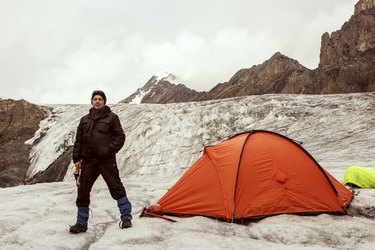 The climber standing near tent on glacier