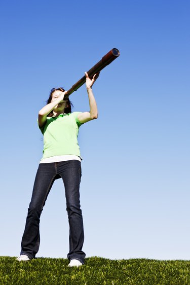 Cute brunette in field looks through antique telescope